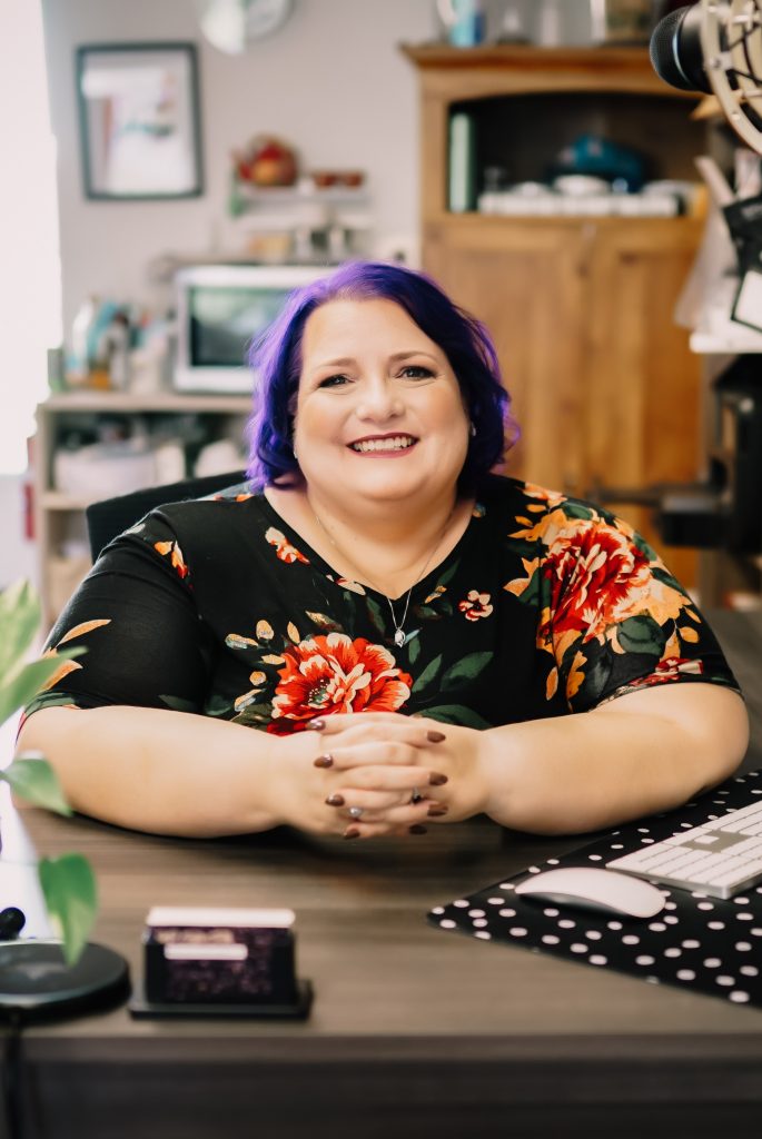 Michelle seated at her desk, hands folded, looking into the camera.